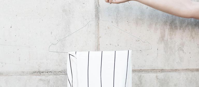 Foto van een witte broek op een kledinghanger voor een betonnen muur 