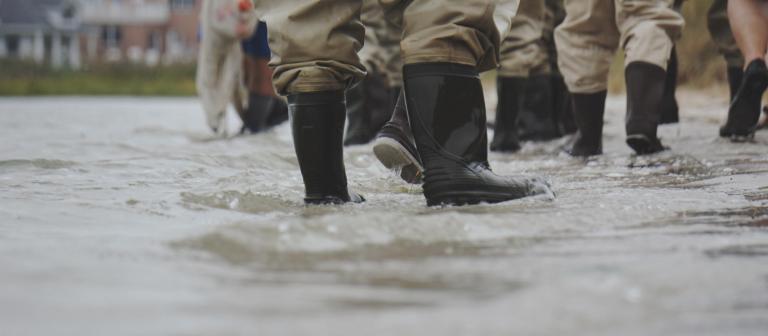 Foto van mensen die met laarzen en regenkleding in een overstroomde straat vol water staan