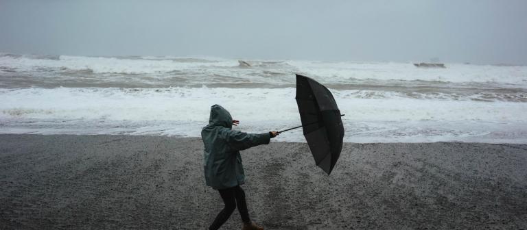 Foto van persoon met paraplu op het strand in een storm
