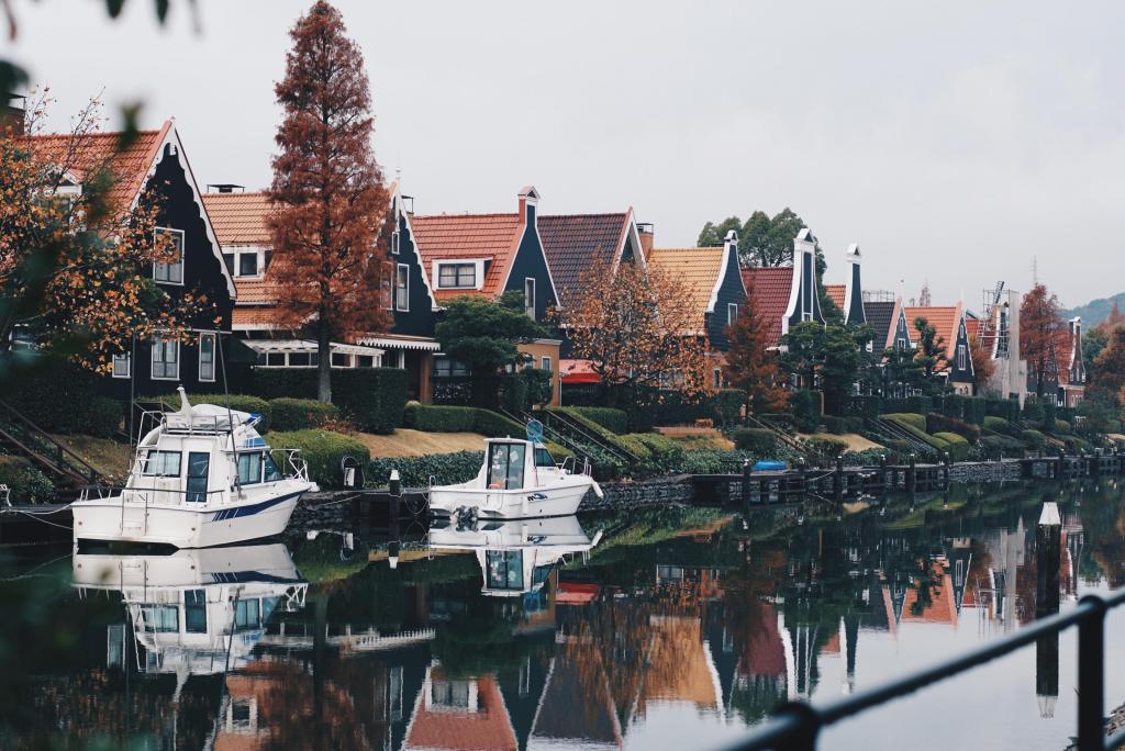 Foto van een rij huizen met een rivier ervoor waar bootjes in liggen