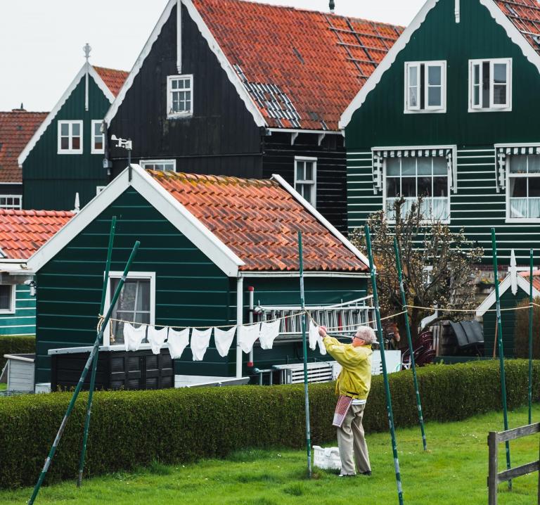 Foto van een persoon die de was ophangt met de op de achtergrond typisch Nederlands Zaanse huizen