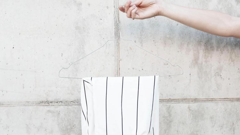Foto van een witte broek op een kledinghanger voor een betonnen muur 