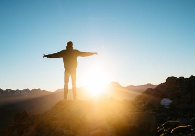 Foto van een man op een bergtop die zijn armen strekt tijdens zonsopgang